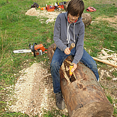 Kind bearbeitet liegenden Baumstamm mit einem Beitel