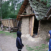 Kind steht vor einem Lehmhaus und einem Leiterwagen